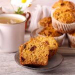 Carrot raisin muffin sliced in half and presented on gray plate with mug of hot tea in background.